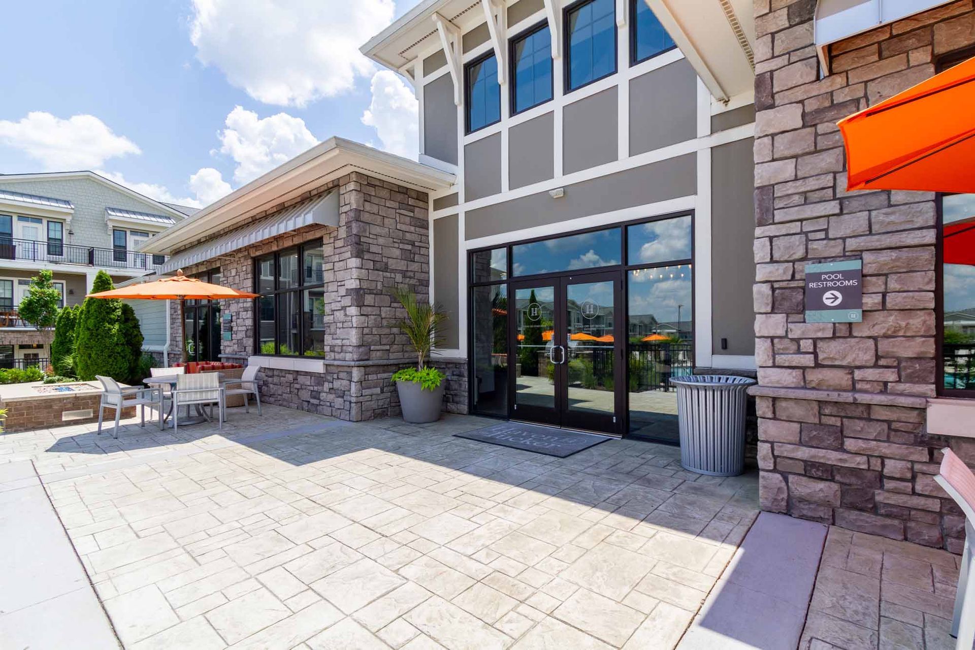 Patio of a building with stone and gray siding, glass doors, and orange umbrellas.