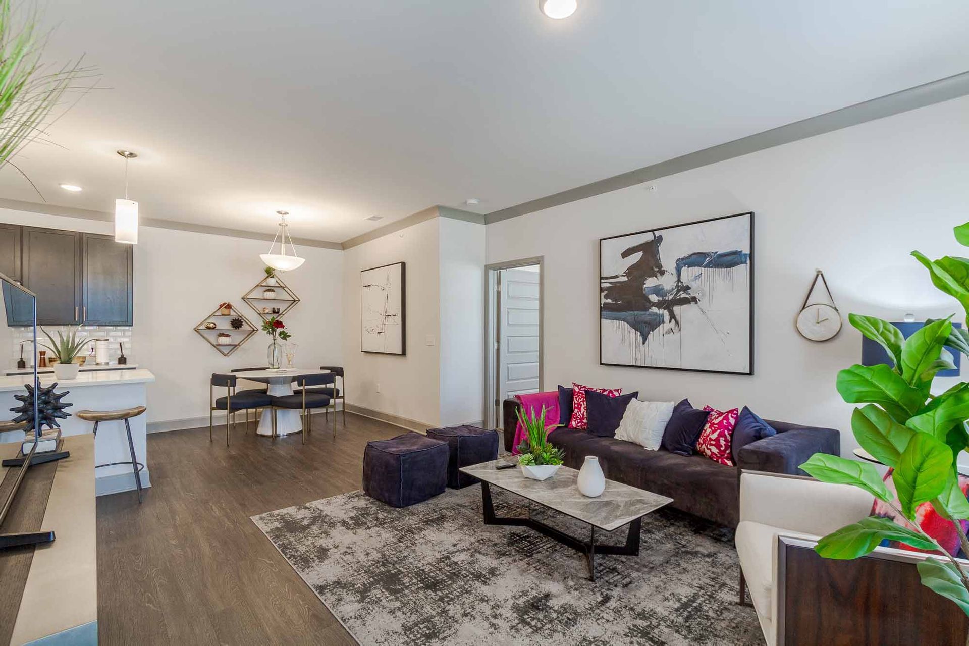 Modern living room with dark gray flooring, open to a dining area and kitchen; sofa and rug.
