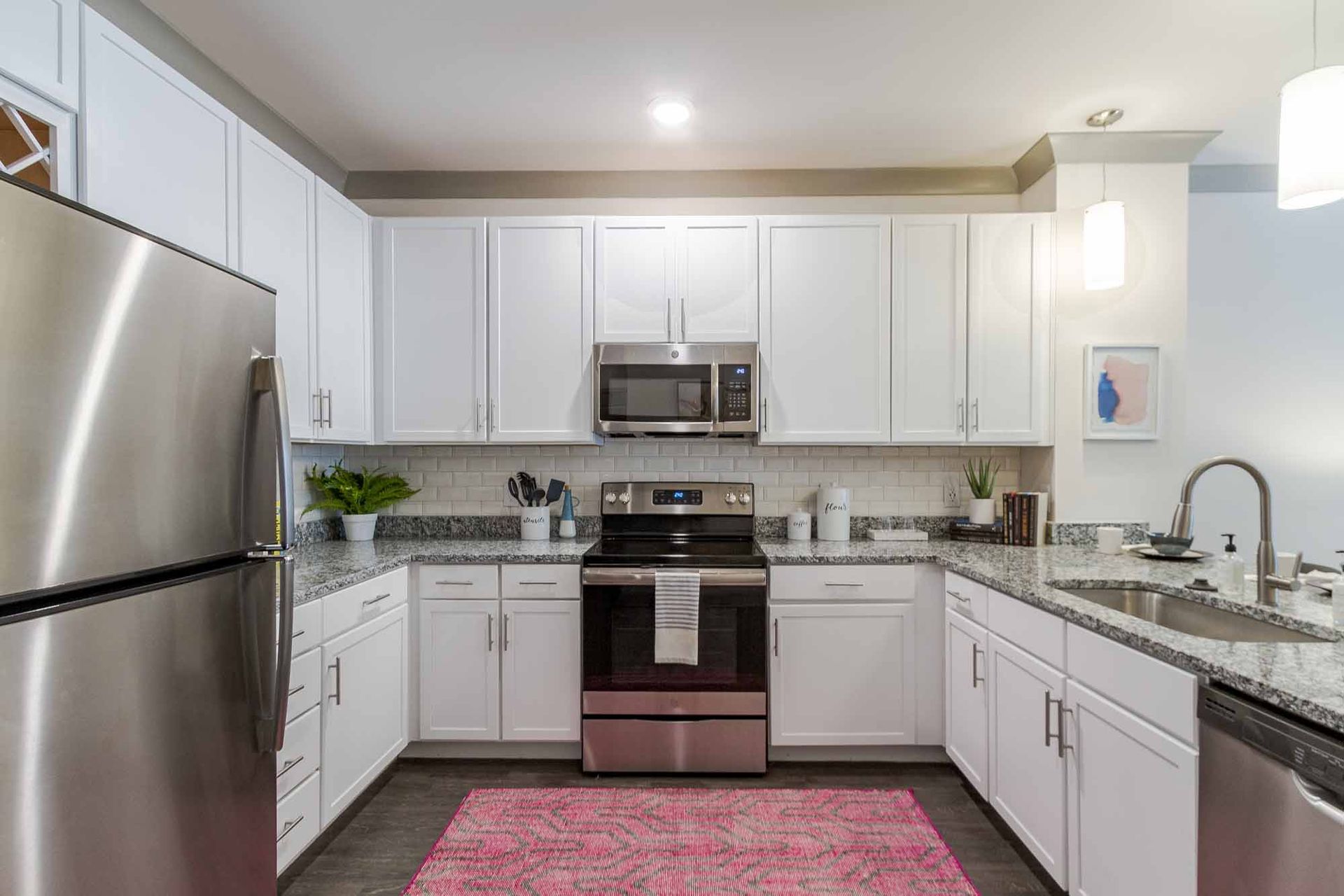 Modern white kitchen with stainless steel appliances, granite countertops, and a pink rug.