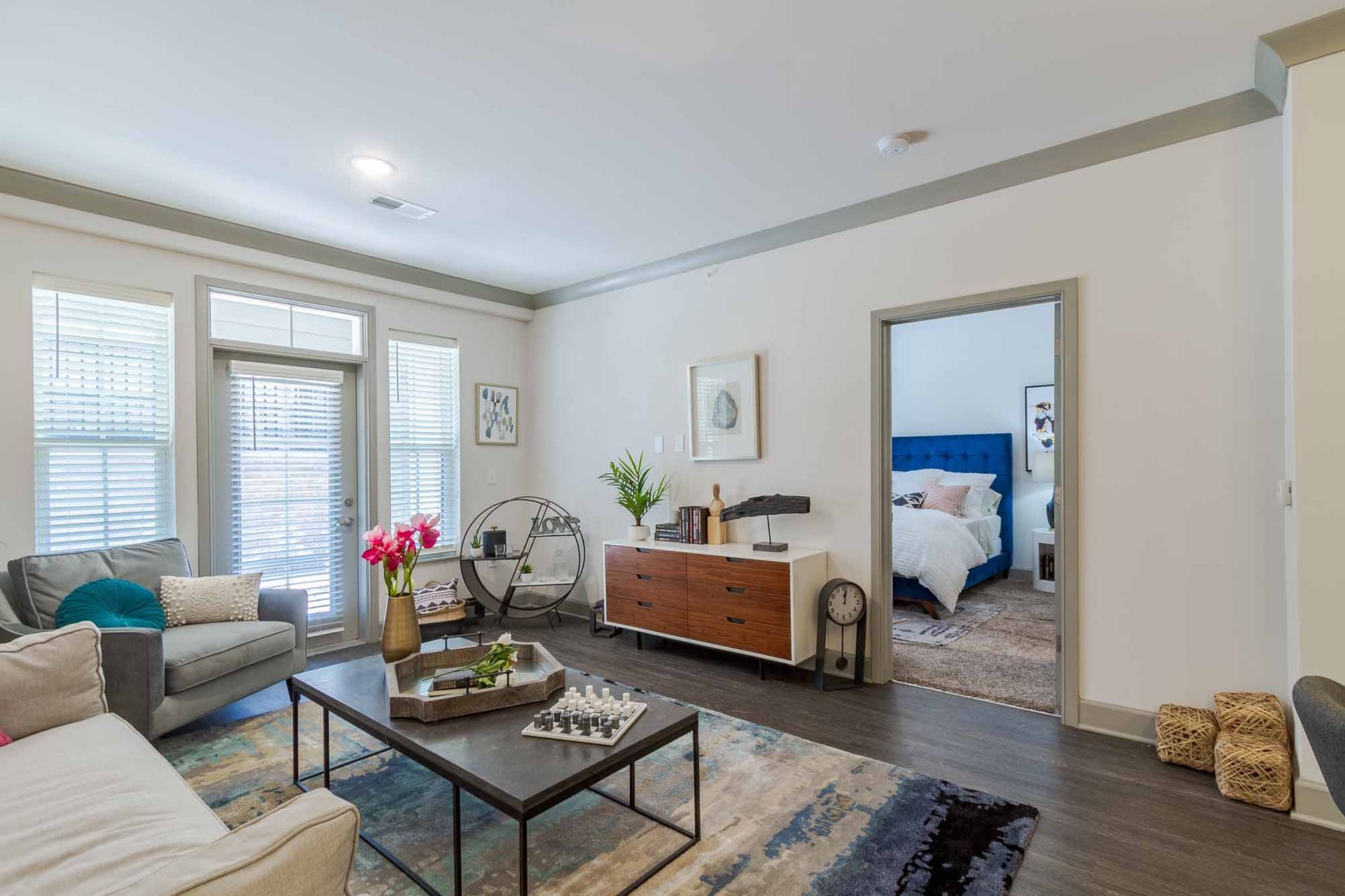 Living room with gray sofa, wooden cabinet, and view of a bedroom.