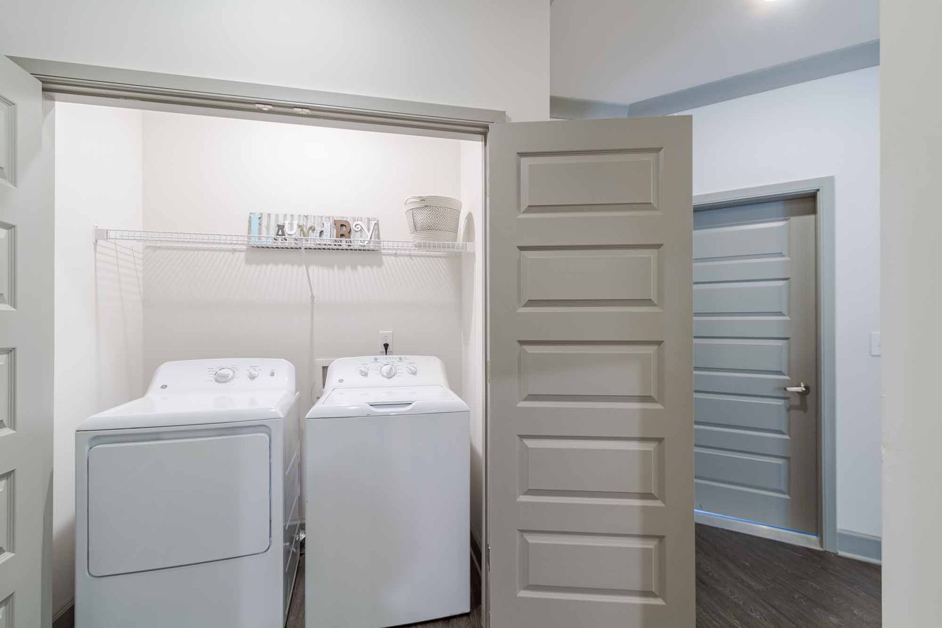 Laundry room with white washer and dryer, open door, and adjacent door.