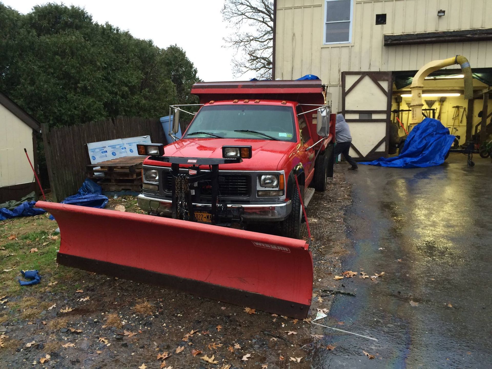 Red pickup truck with snowplow parked in front of a building. Person is near the garage door.