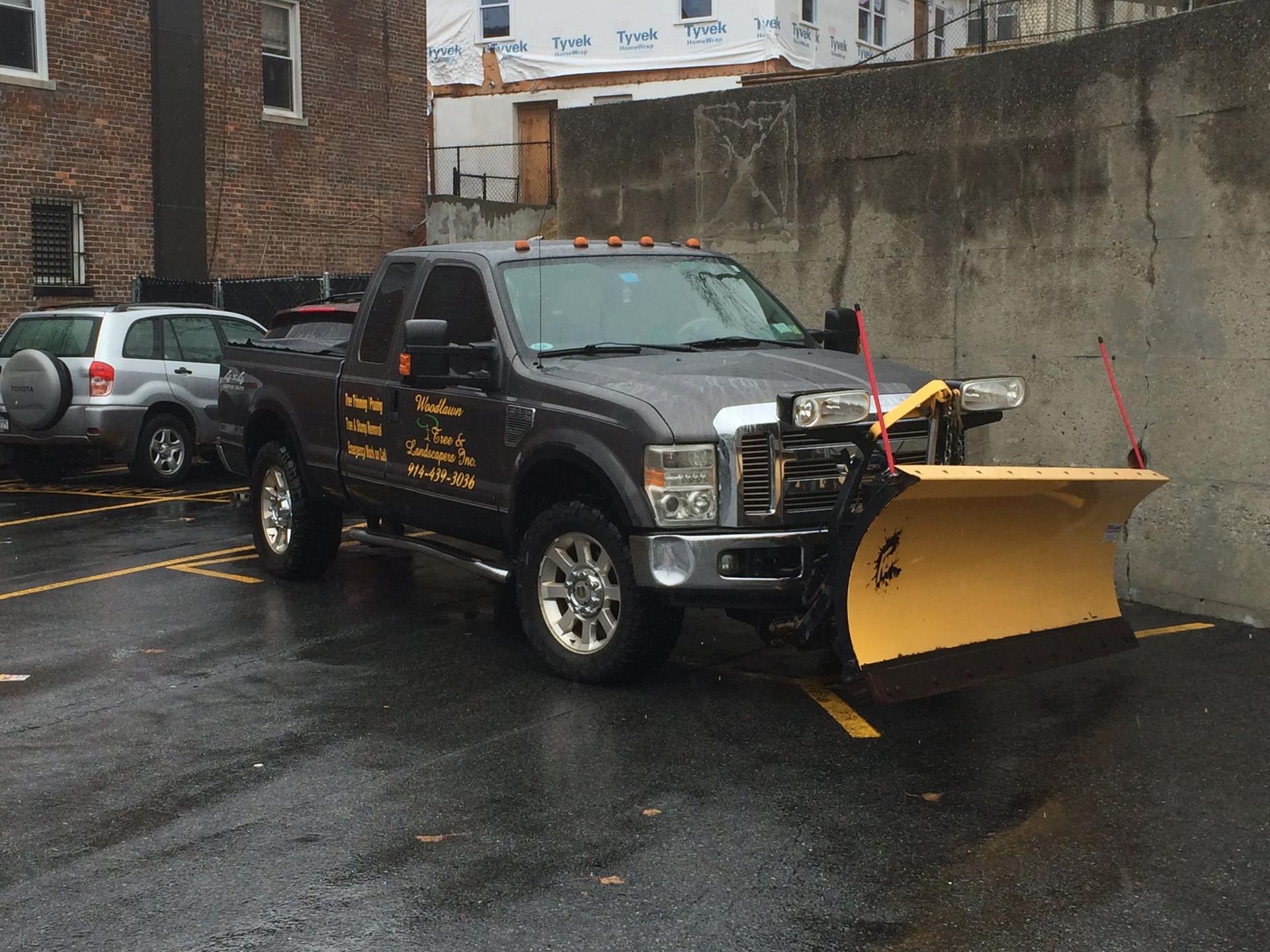 Dark pickup truck with a yellow snowplow parked on wet asphalt.