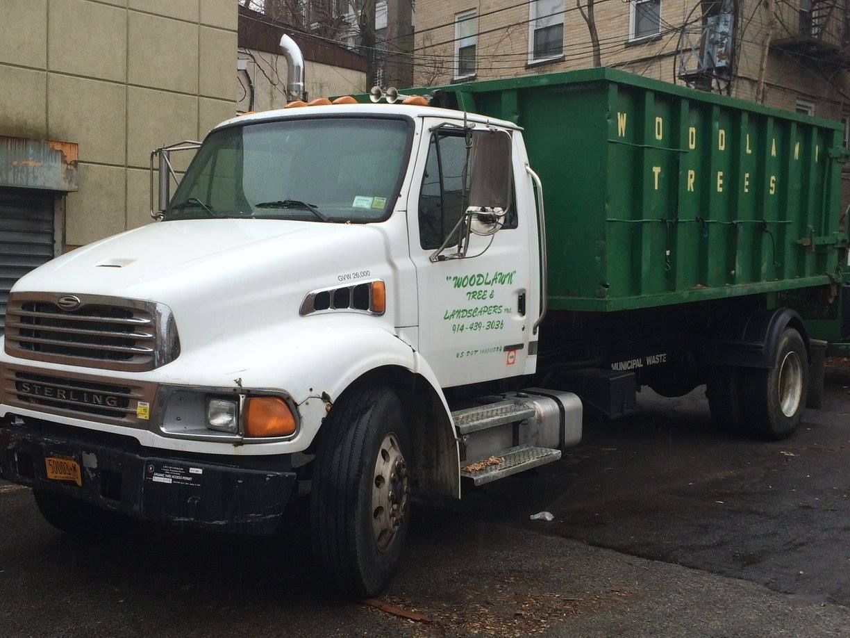 White Sterling truck with green dumpster on a city street.