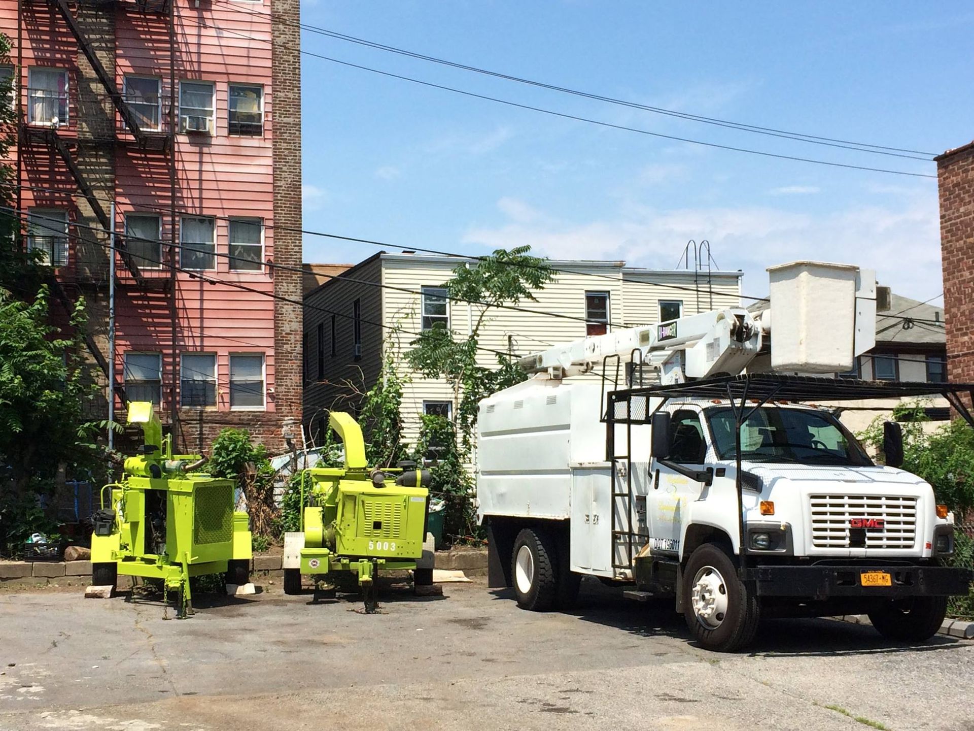 Green chippers and a white utility truck parked by a red brick building, clearing debris.