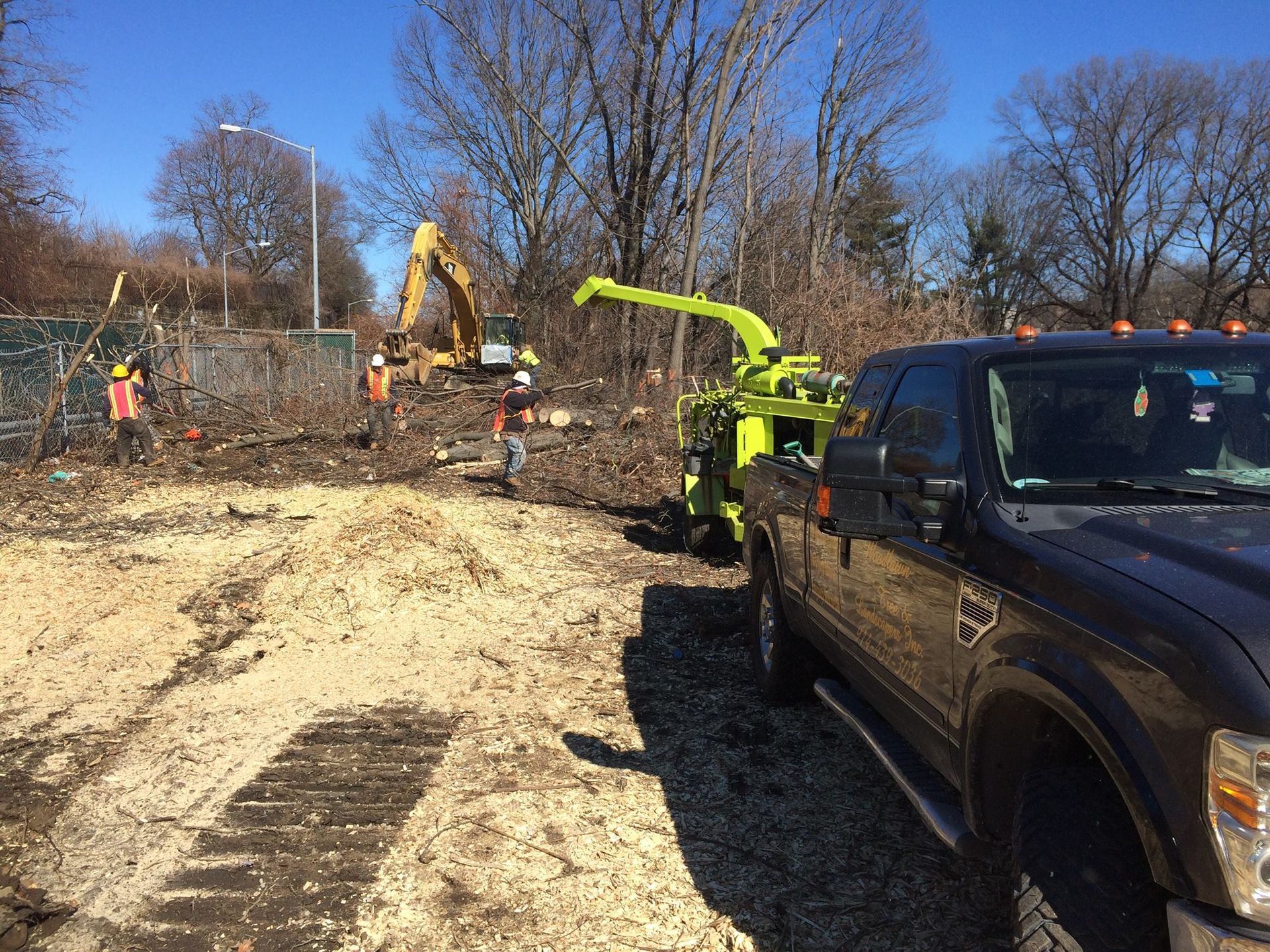 Truck next to a wood chipper; workers clearing brush with an excavator on a sunny day.