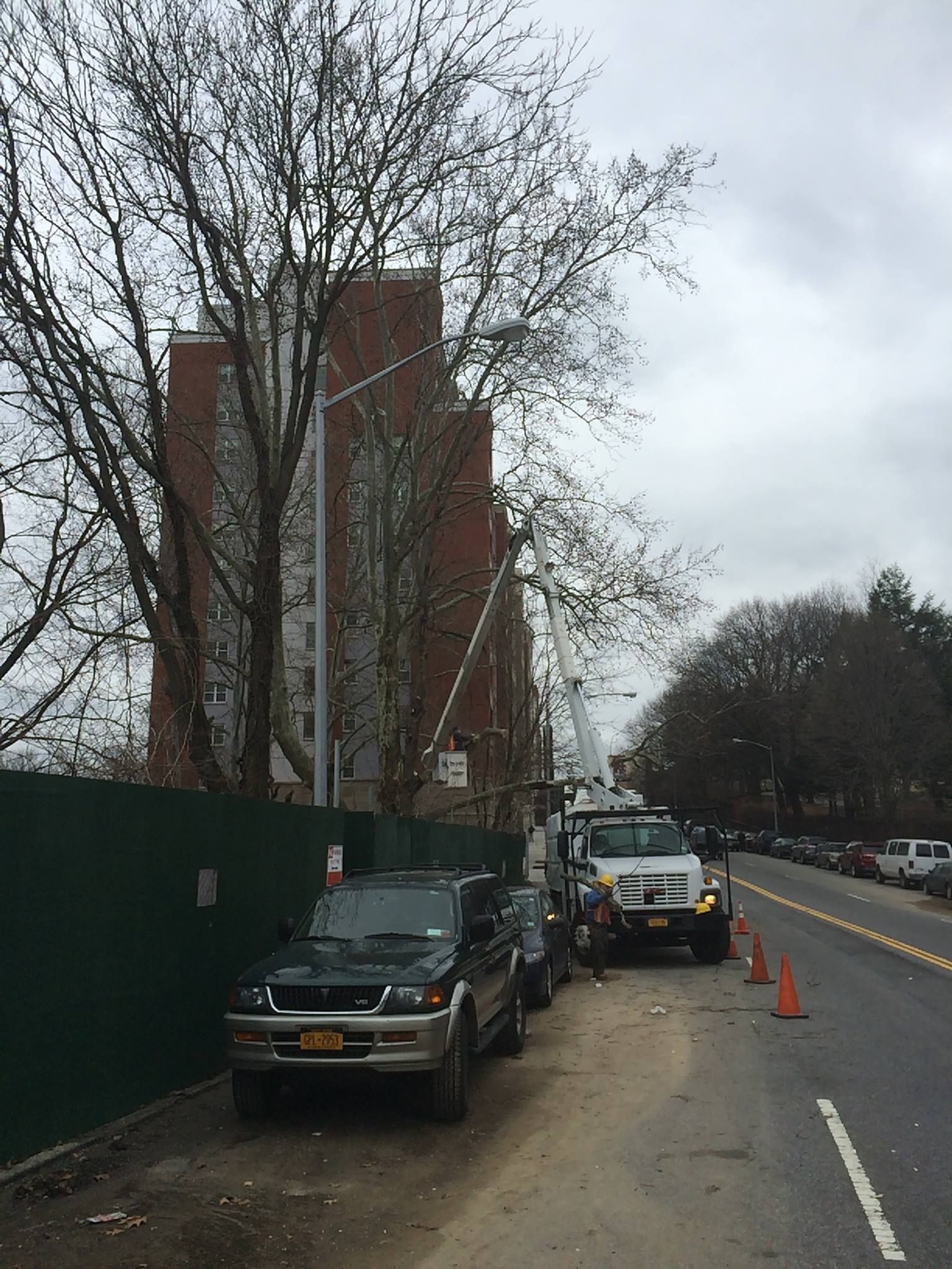 Cars parked on a street next to a tall brick building and a green construction fence.