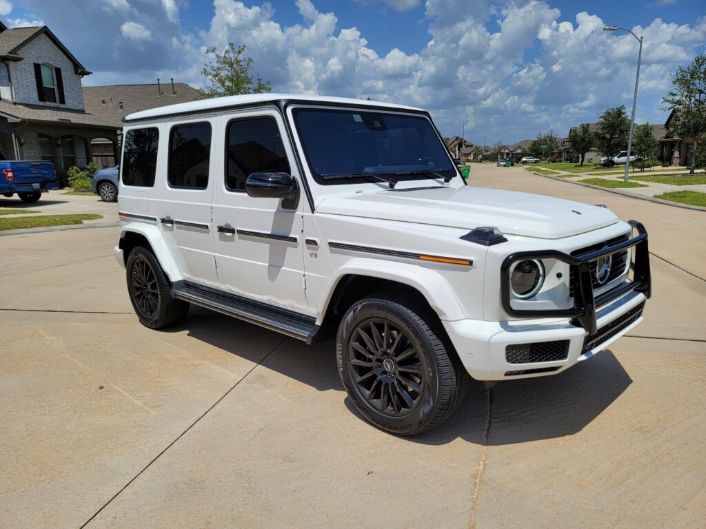 A white mercedes benz g class is parked in a driveway in front of a house.