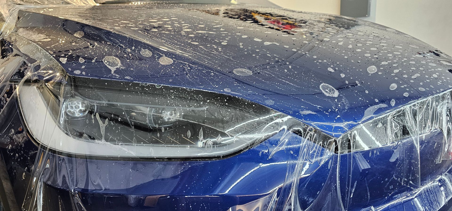 A person is cleaning the windshield of a blue car.