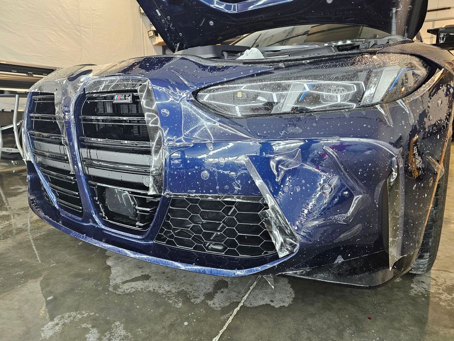Blue car with clear protective film on the front. Hood is open.