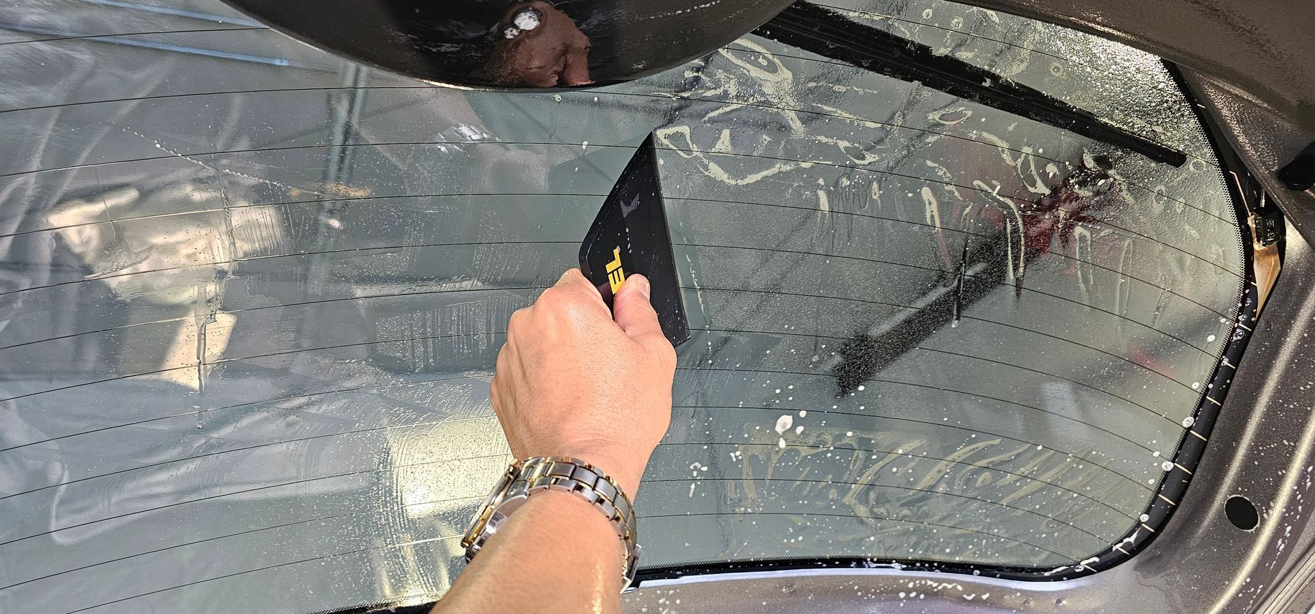 A person is cleaning a car windshield with a squeegee.