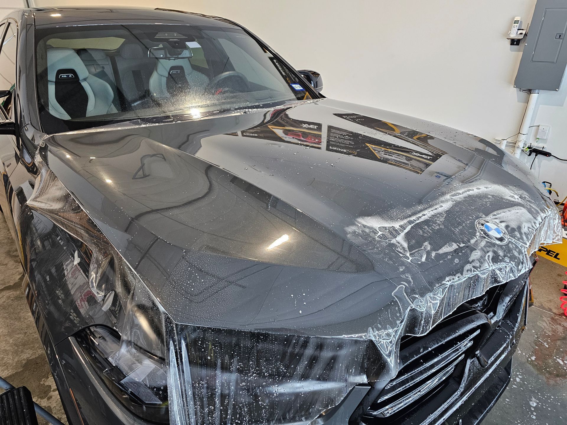 Dark gray car with a clear protective film on the hood in a garage.
