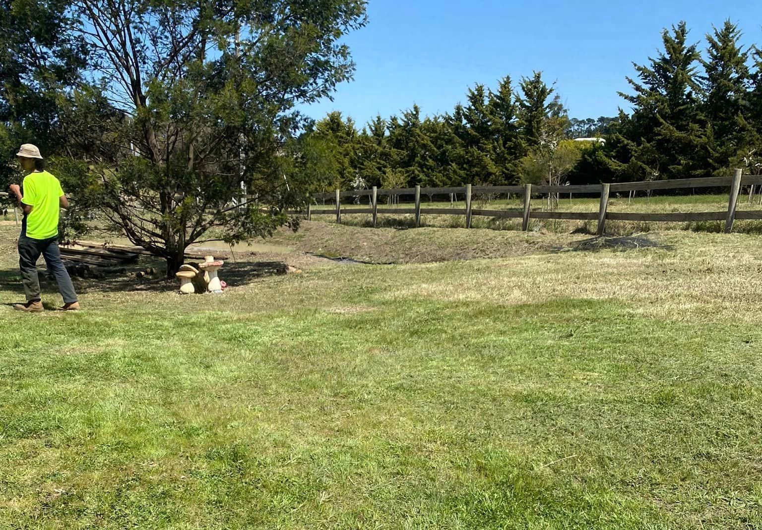 A man in a yellow shirt is standing in a grassy field. — Hayman Acres Garden Services In Echuca, VIC