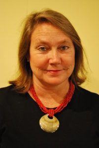 A woman wearing a black shirt and a red necklace is smiling for the camera.
