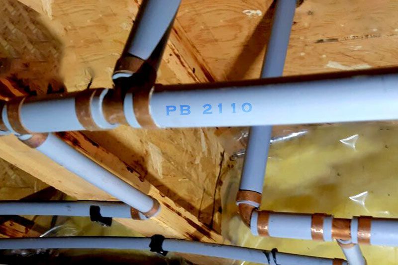 Blue PB 2110 pipes and copper fittings installed in a wooden attic with insulation.
