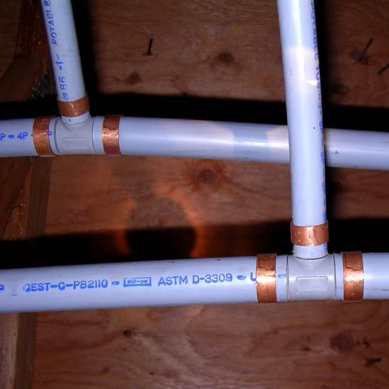 PVC pipes with copper couplings, installed against a wooden wall.