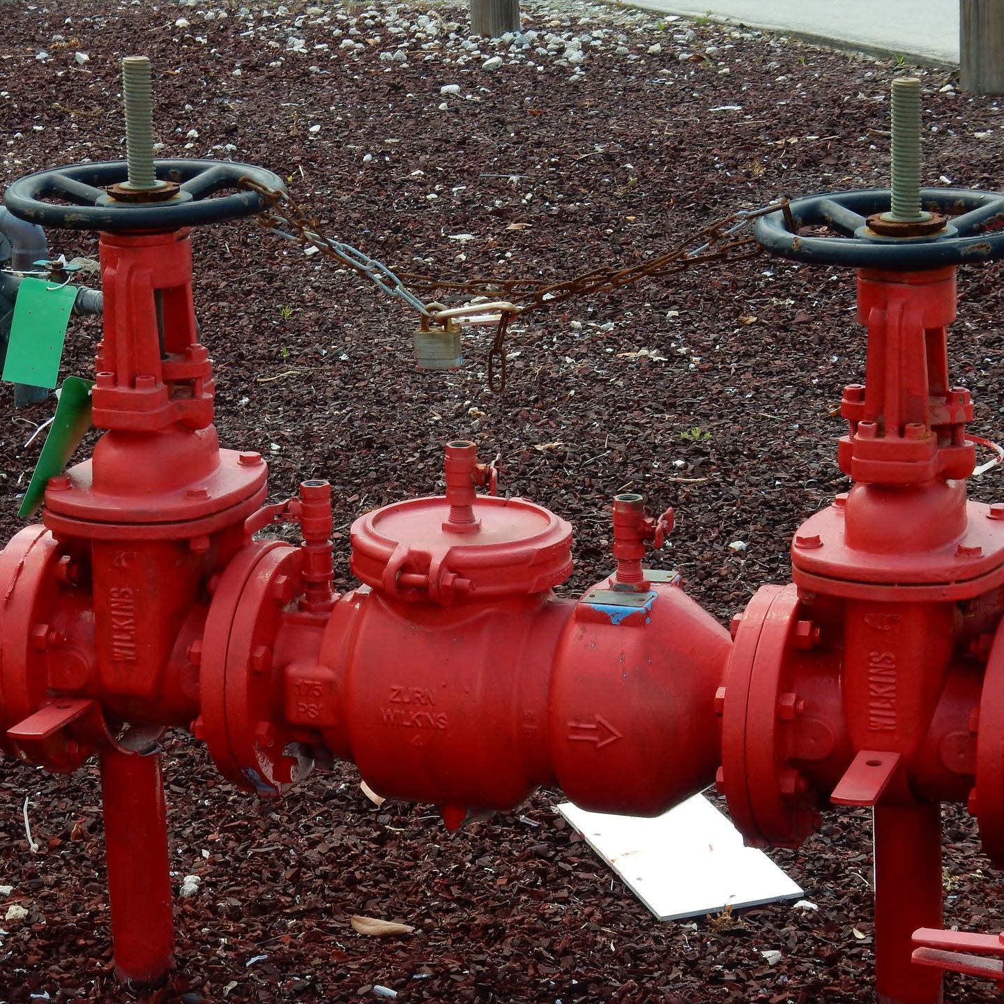 Red water valves in an outdoor setting with a brown, gravel-like ground cover.