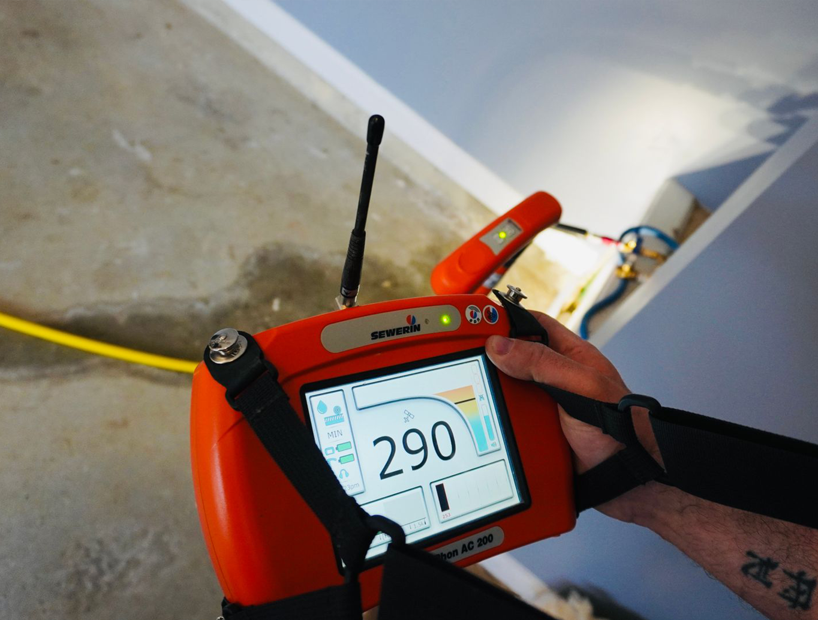 Person holding an orange diagnostic device, possibly for water leak detection, in a construction setting.