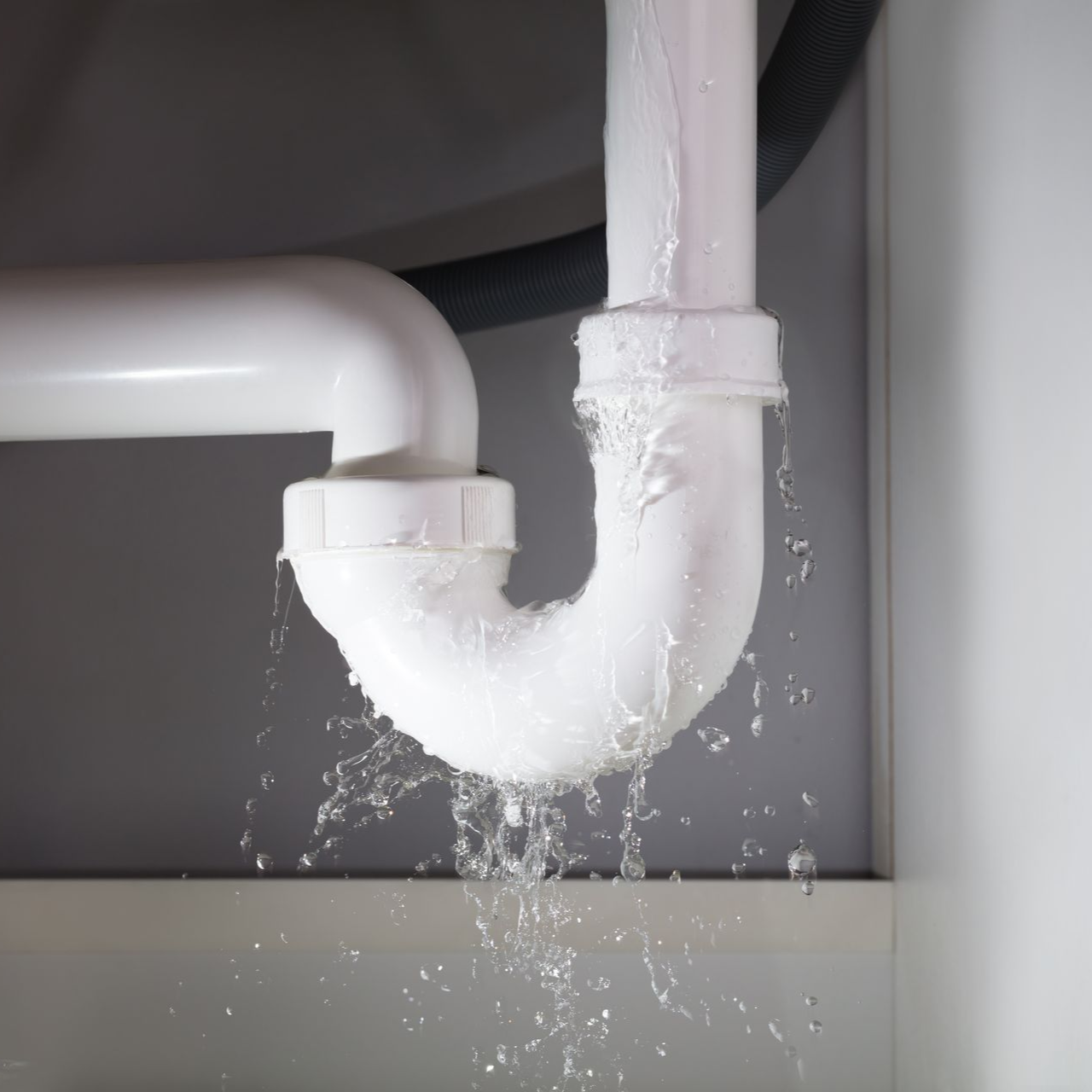 Leaking white plumbing pipe under a sink, water spilling out.