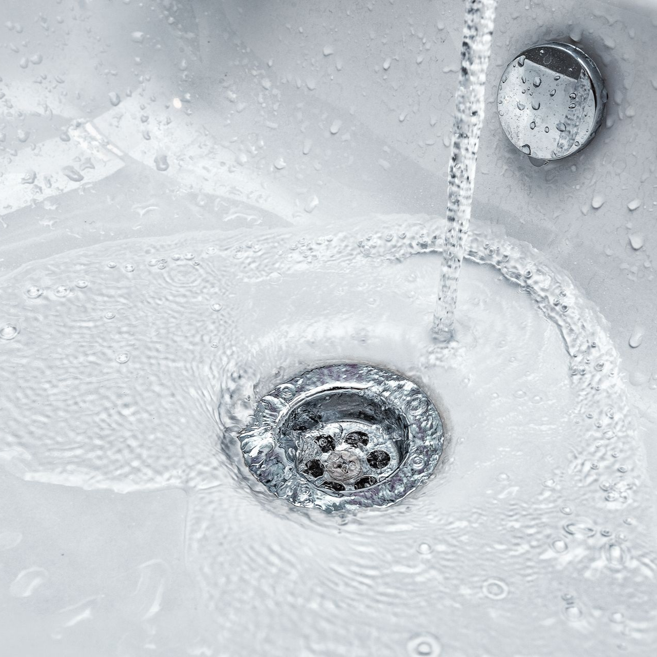 Water running into a white sink, flowing towards the drain.