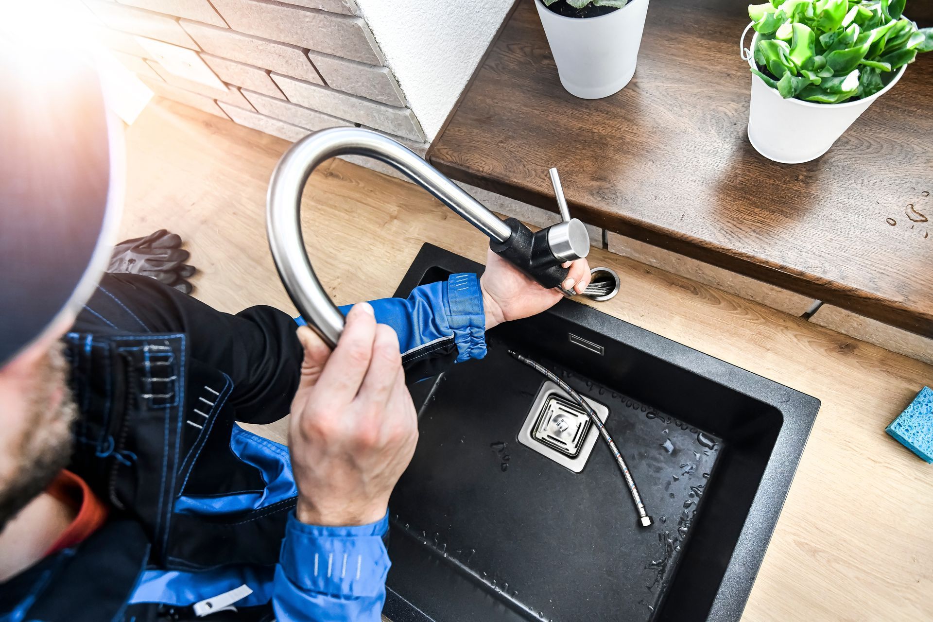 Plumber installing a new kitchen sink faucet in a black sink, with a countertop in the background.