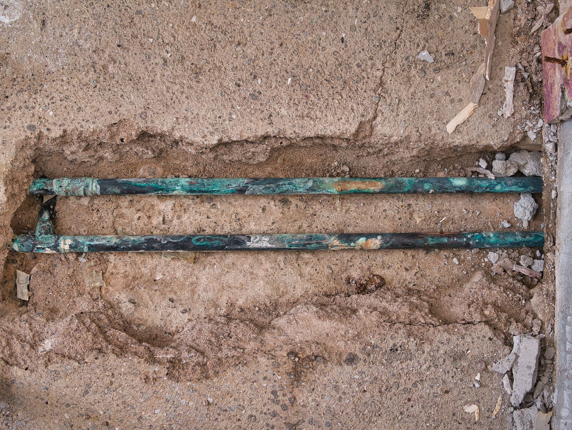 Two corroded copper pipes embedded in a rough concrete wall.