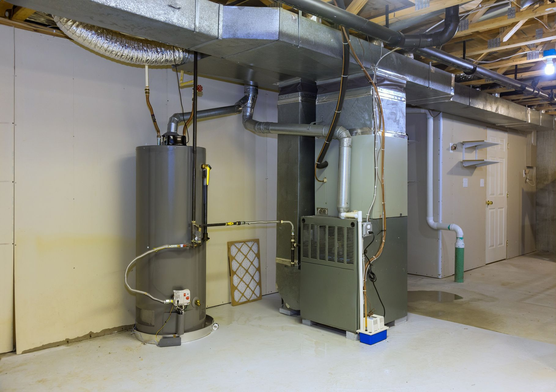 Water heater and furnace in a basement utility room with ductwork overhead.