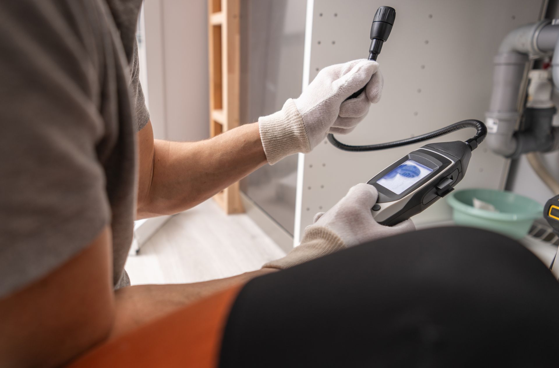 Person in gloves using a borescope to inspect plumbing under a sink.
