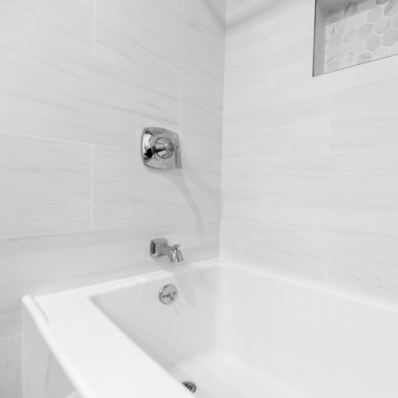 White bathtub with chrome fixtures, set in a tiled bathroom with a recessed shelf.
