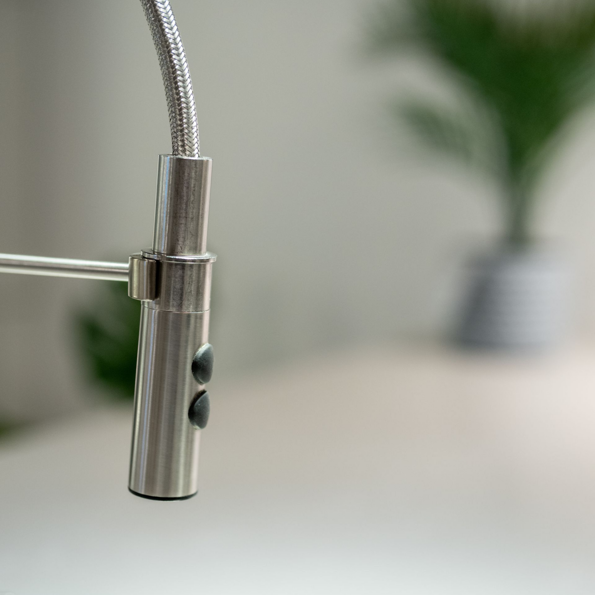 Close-up of a stainless steel kitchen faucet with two black buttons and a coiled hose.