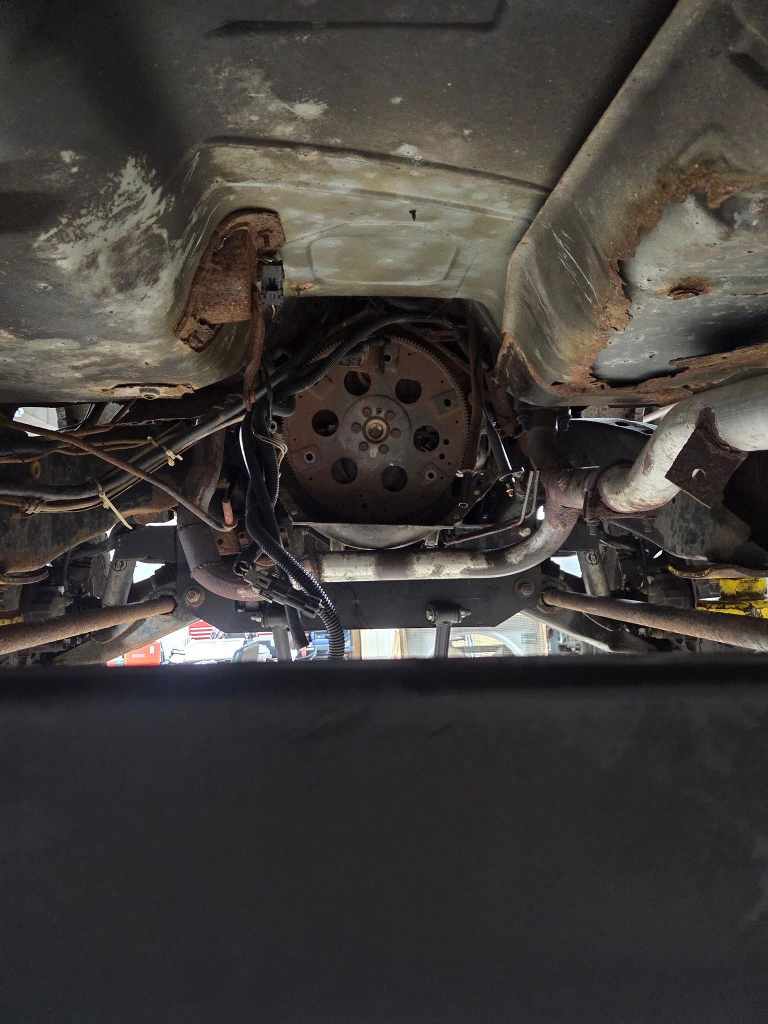 Undercarriage of a vehicle showing a rusted transmission and exhaust system.