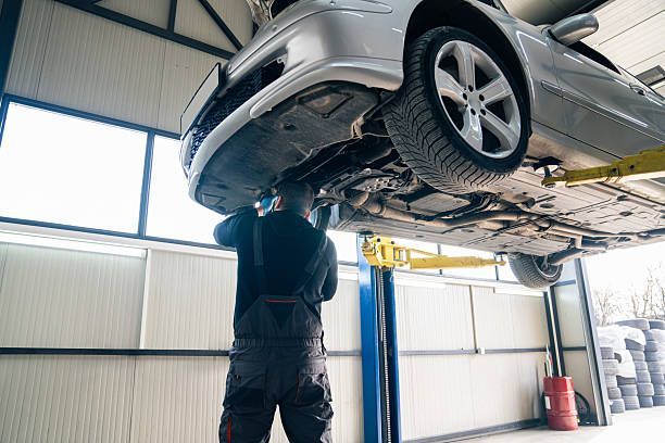 Mechanic working on the underside of a car lifted in a garage.