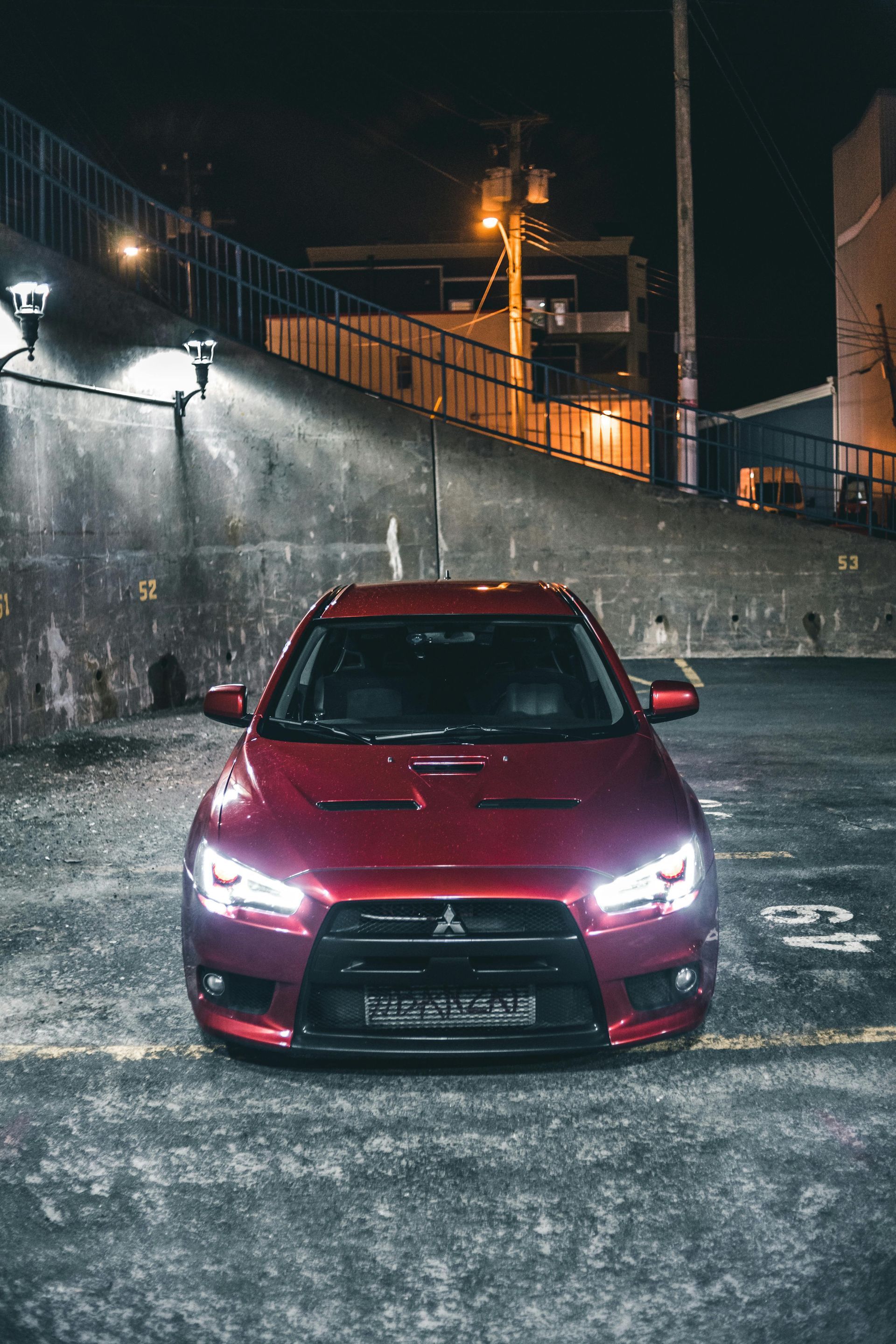 Red Mitsubishi Lancer Evolution parked at night, lit by streetlights.