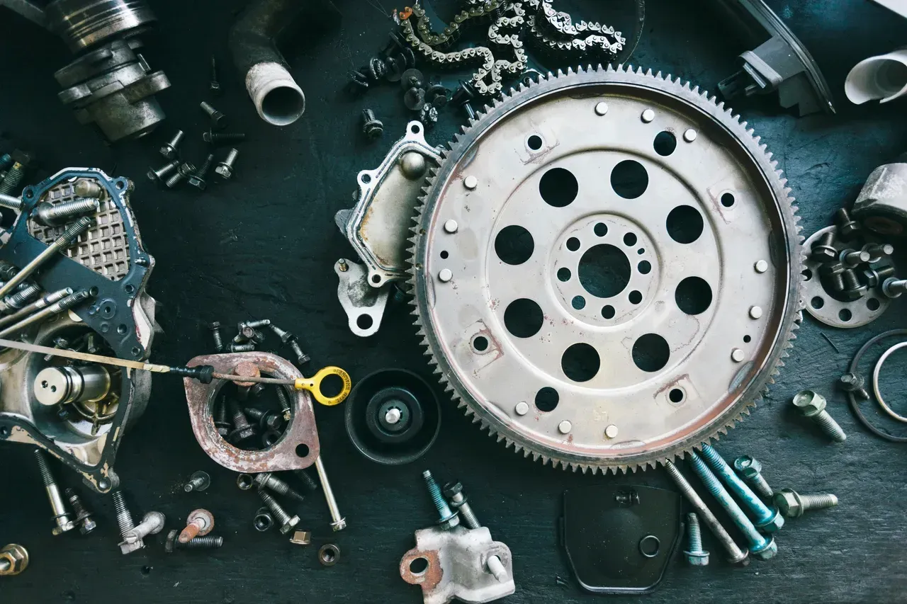 Car parts scattered on a dark surface, including a gear, bolts, and other mechanical components.