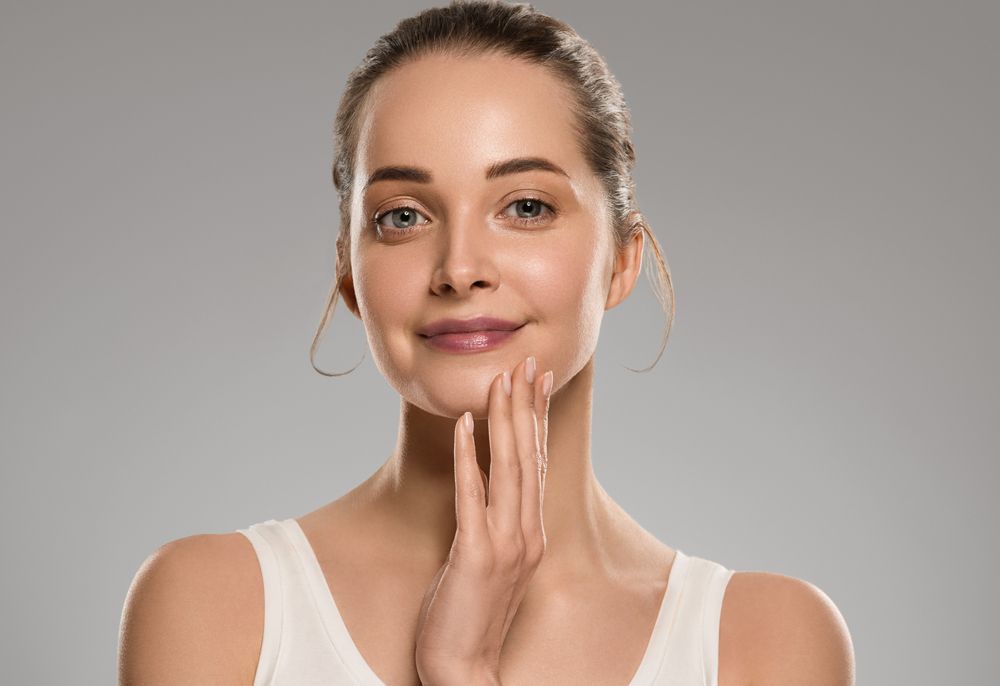 A woman is touching her face with her hands and smiling.