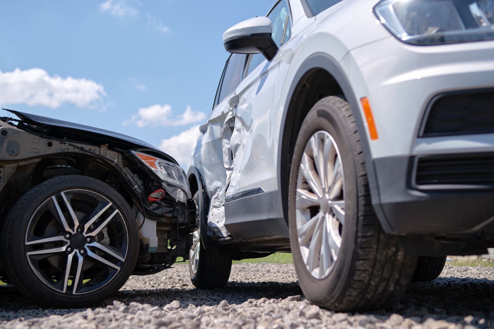 A white SUV with heavy side-impact damage parked on gravel after a collision with the front end of a dark-colored car.