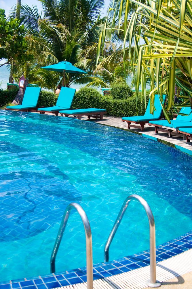 A Large Swimming Pool Surrounded By Blue Chairs And Umbrellas — Yamba Pools & Spas In Yamba, NSW
