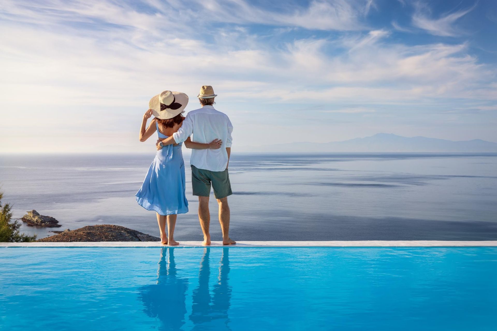 A Man And A Woman Are Standing Next To A Swimming Pool Overlooking The Ocean — Yamba Pools & Spas In Yamba, NSW