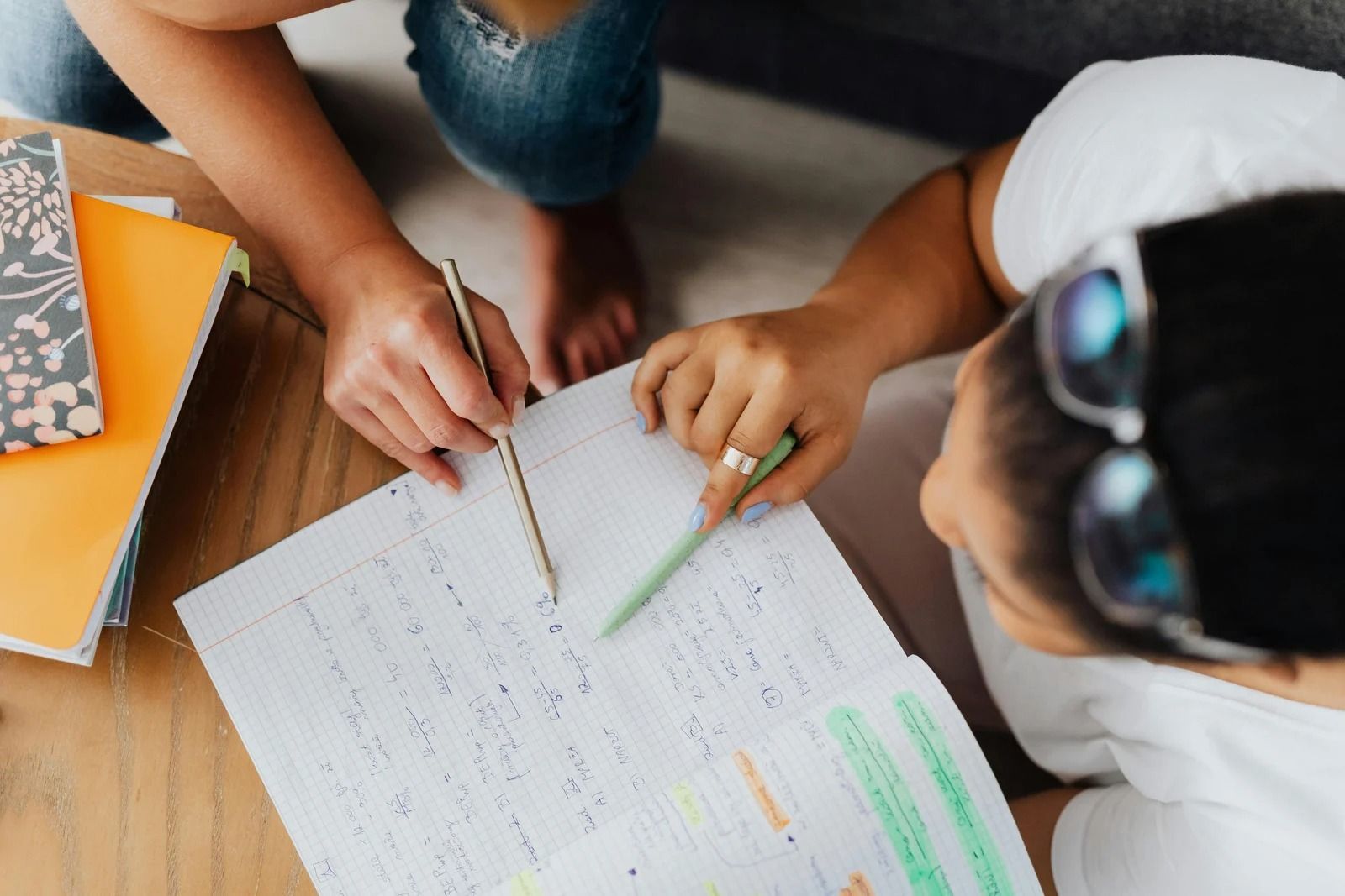 Two people sit at a table, using pens to work on a handwritten document together.