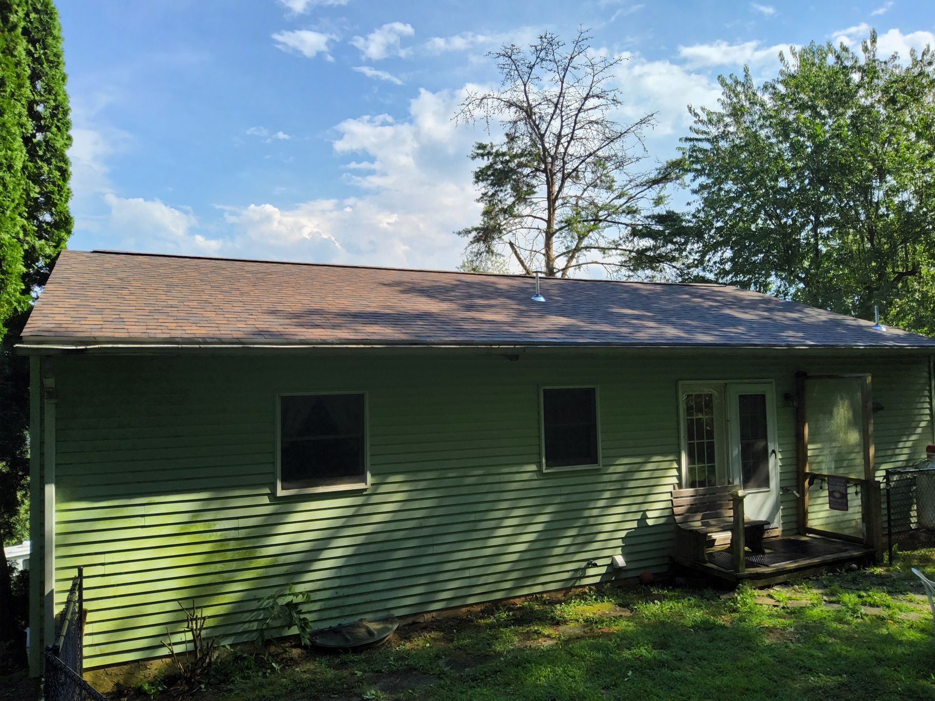 A green house with a brown roof is sitting in the middle of a lush green field.
