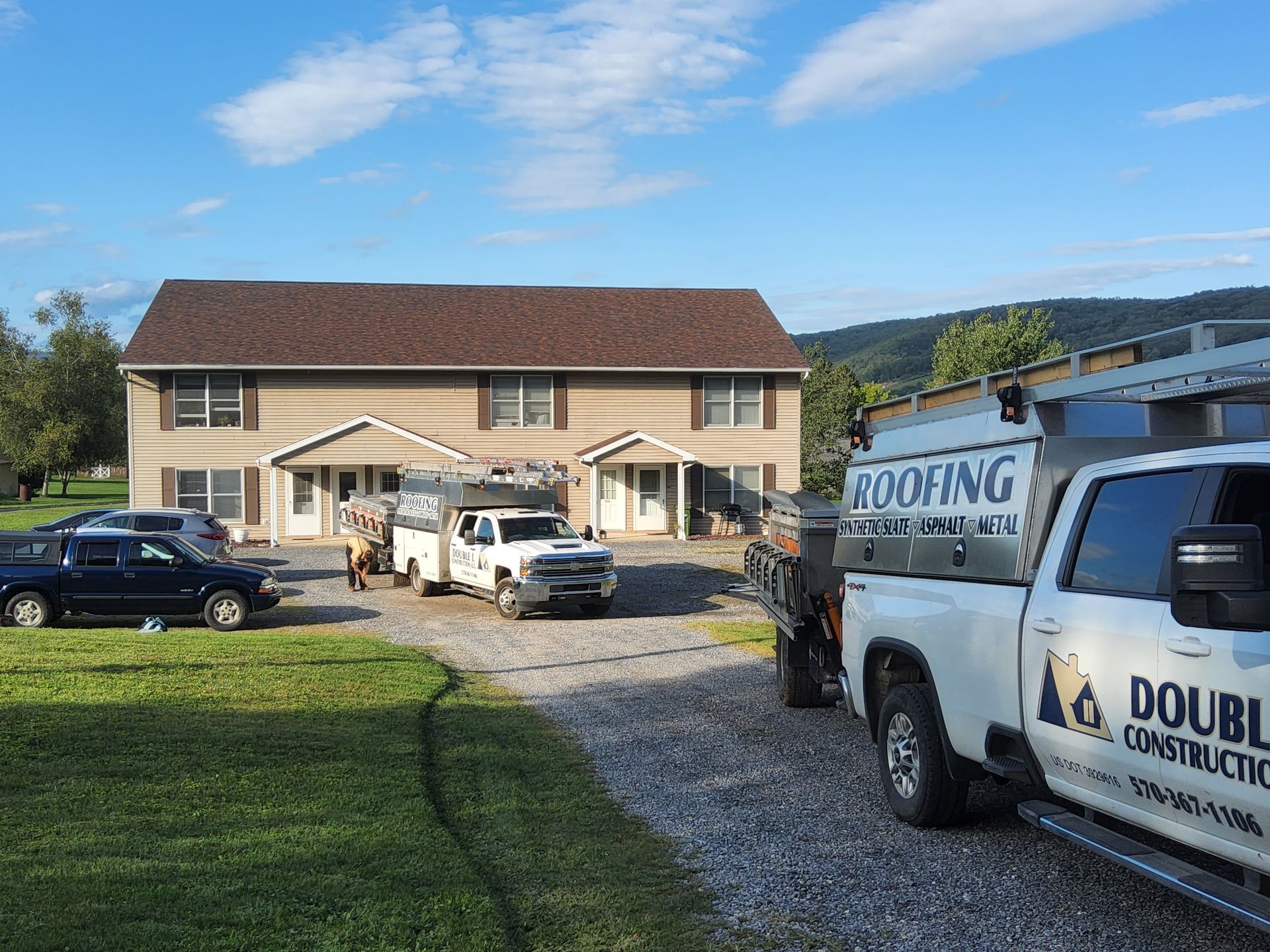 Two roofing trucks are parked in front of a house.