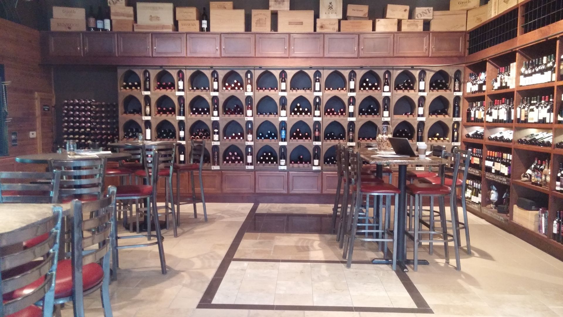 A restaurant with tables and chairs in front of a wall of wine bottles
