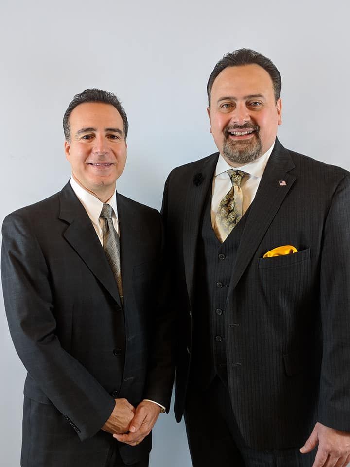 Two men in suits and ties are standing next to each other and smiling.