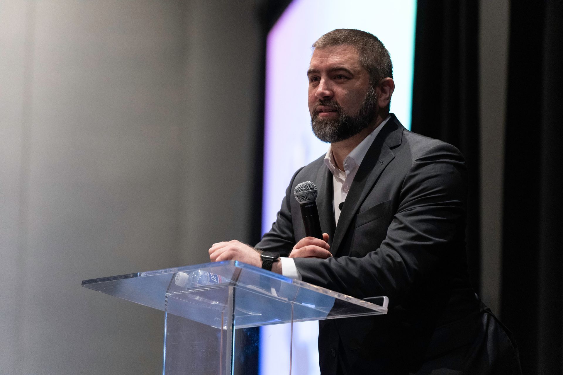 A man in a suit is standing at a podium holding a microphone.