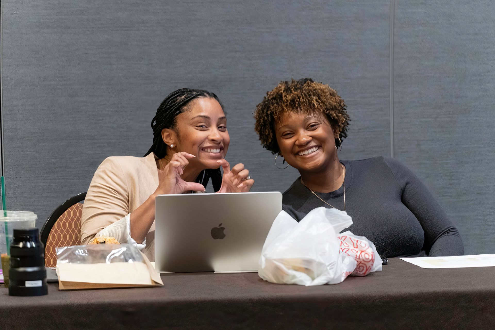 Two women are sitting at a table looking at a laptop computer.