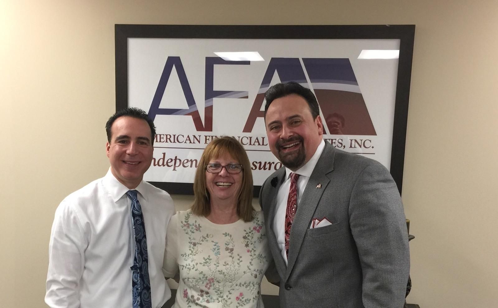 Three people are posing for a picture in front of a sign that says afa