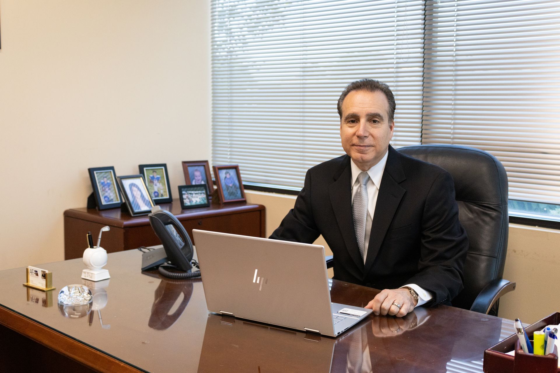 A man in a suit and tie is sitting at a desk with a laptop.