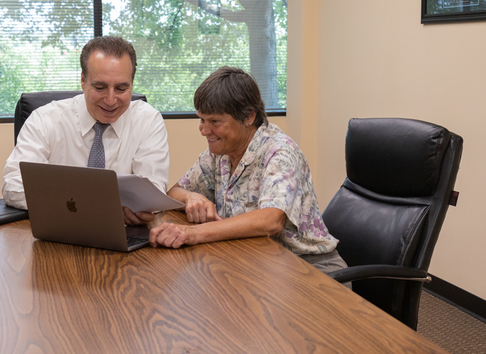 A man and a woman are sitting at a table looking at a laptop.