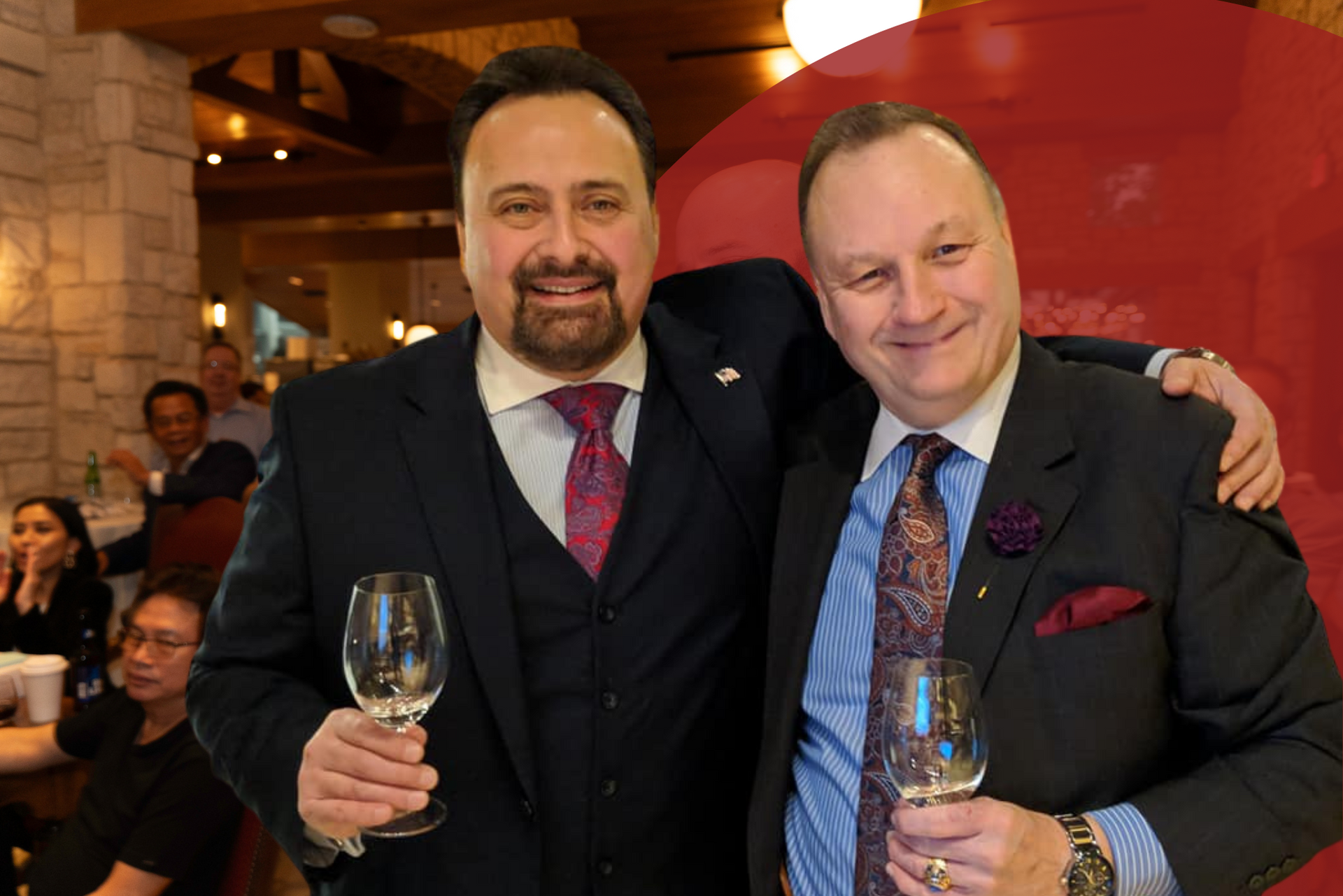 Two men in suits and ties are posing for a picture while holding wine glasses.