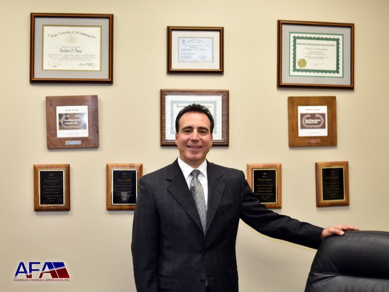 A man in a suit and tie is standing in front of a wall of framed awards